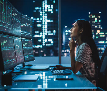 Retrato de uma Analista Financeira Trabalhando em um Computador com Estação de Trabalho Multi-Monitor com Gráficos de Ações, Commodities e Mercado de Câmbio em Tempo Real.
